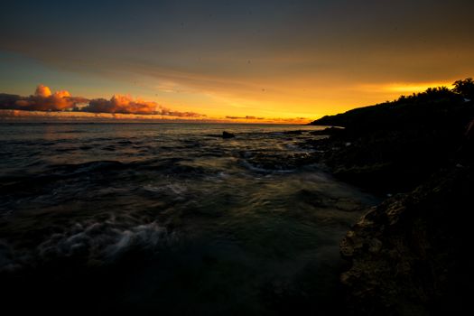 Captivating view of a golden sunset over the ocean with dynamic waves and cloudy sky.