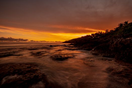 A stunning sunset over a rugged coastline with waves gently hitting the rocks.