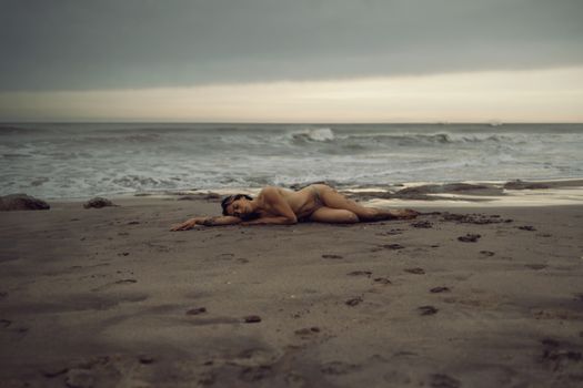 Artistic nude photography capturing tranquility on a moody seaside at dawn.