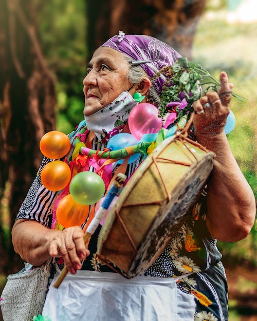 Elderly Woman Dressed in Colorful Clothes Holding a Drum 