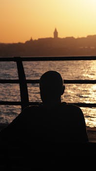 Silhouette of a man watching sunset over water with city skyline in the background.