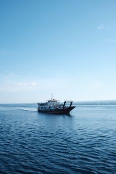 A vessel sailing under a clear blue sky across calm waters, captured vertically.