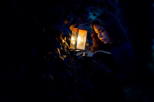 Woman Reading Book near a Kerosene Lamp