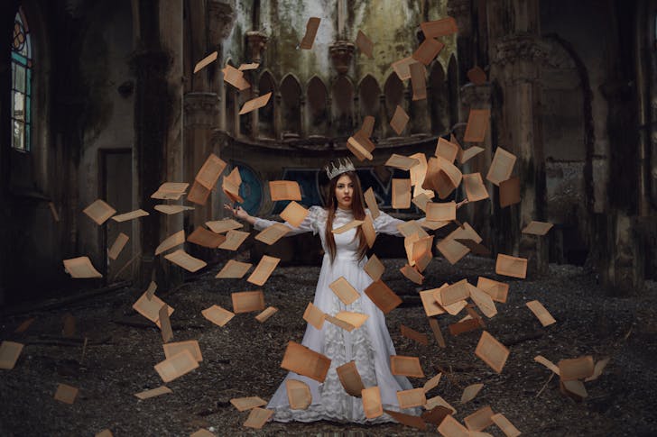 Woman in a Costume and a Crown with Old Yellow Book Pages Flying Around Her 
