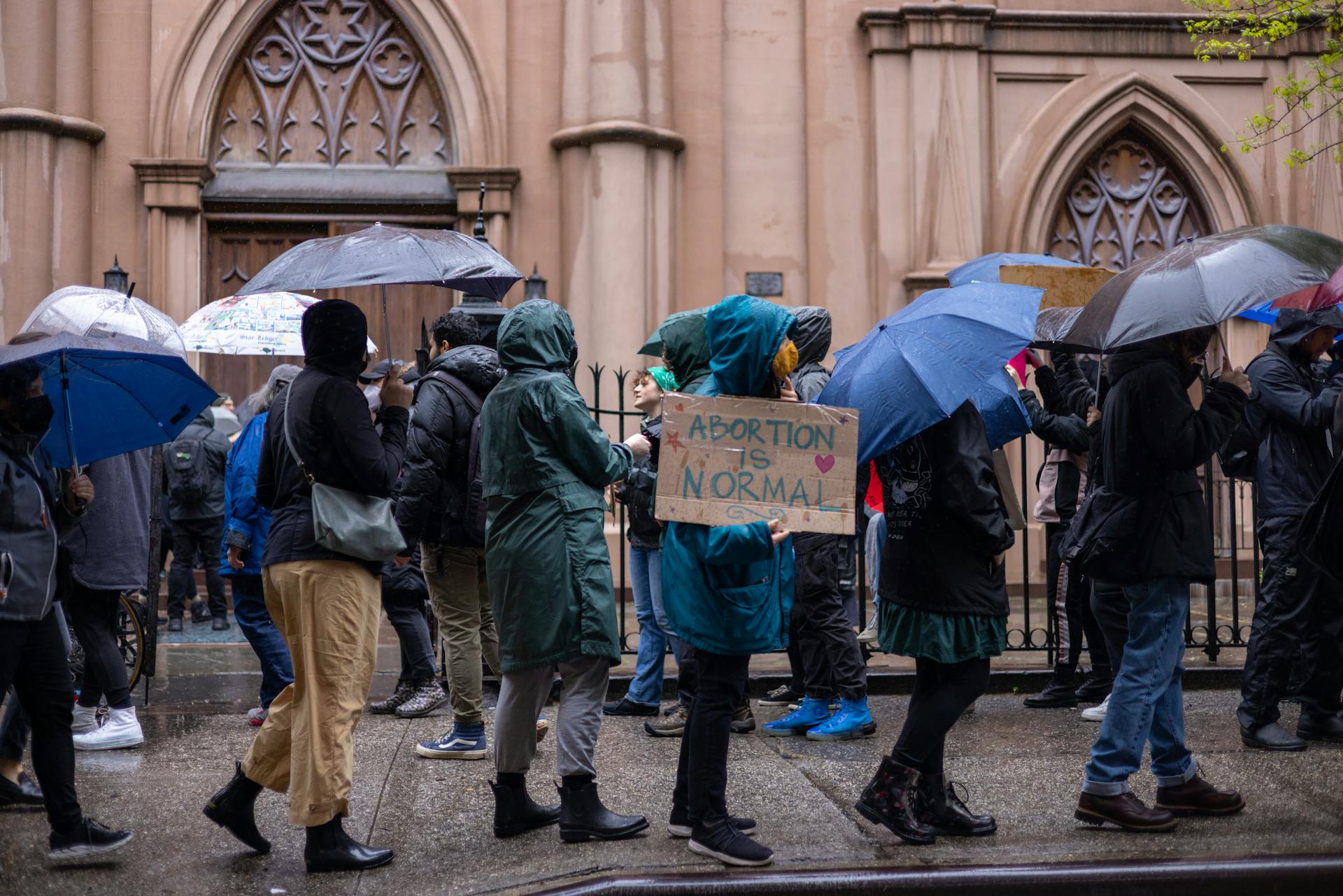 Activists protest for abortion rights in a rainy New York street. Umbrellas and placards visible.