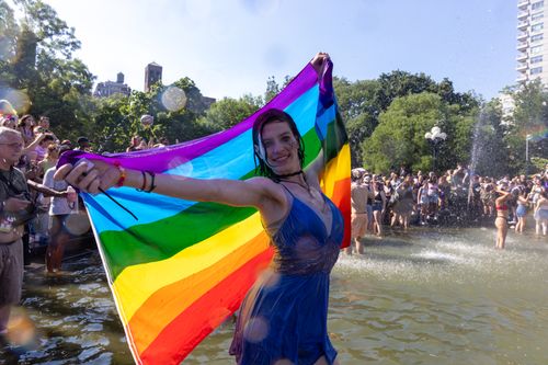Free Joyful celebration at a New York City Pride parade with people around a fountain and rainbow flags. Stock Photo