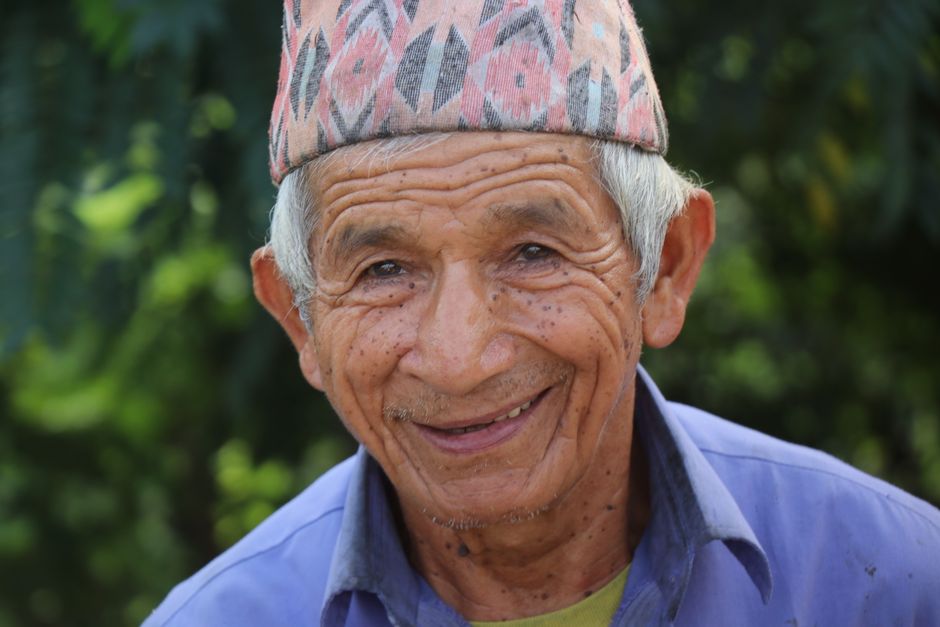 Portrait of an elderly man wearing a traditional dhaka topi, smiling warmly outdoors.