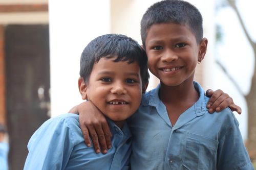 Free Two cheerful boys in blue uniforms, smiling and embracing each other outdoors, showcasing friendship. Stock Photo