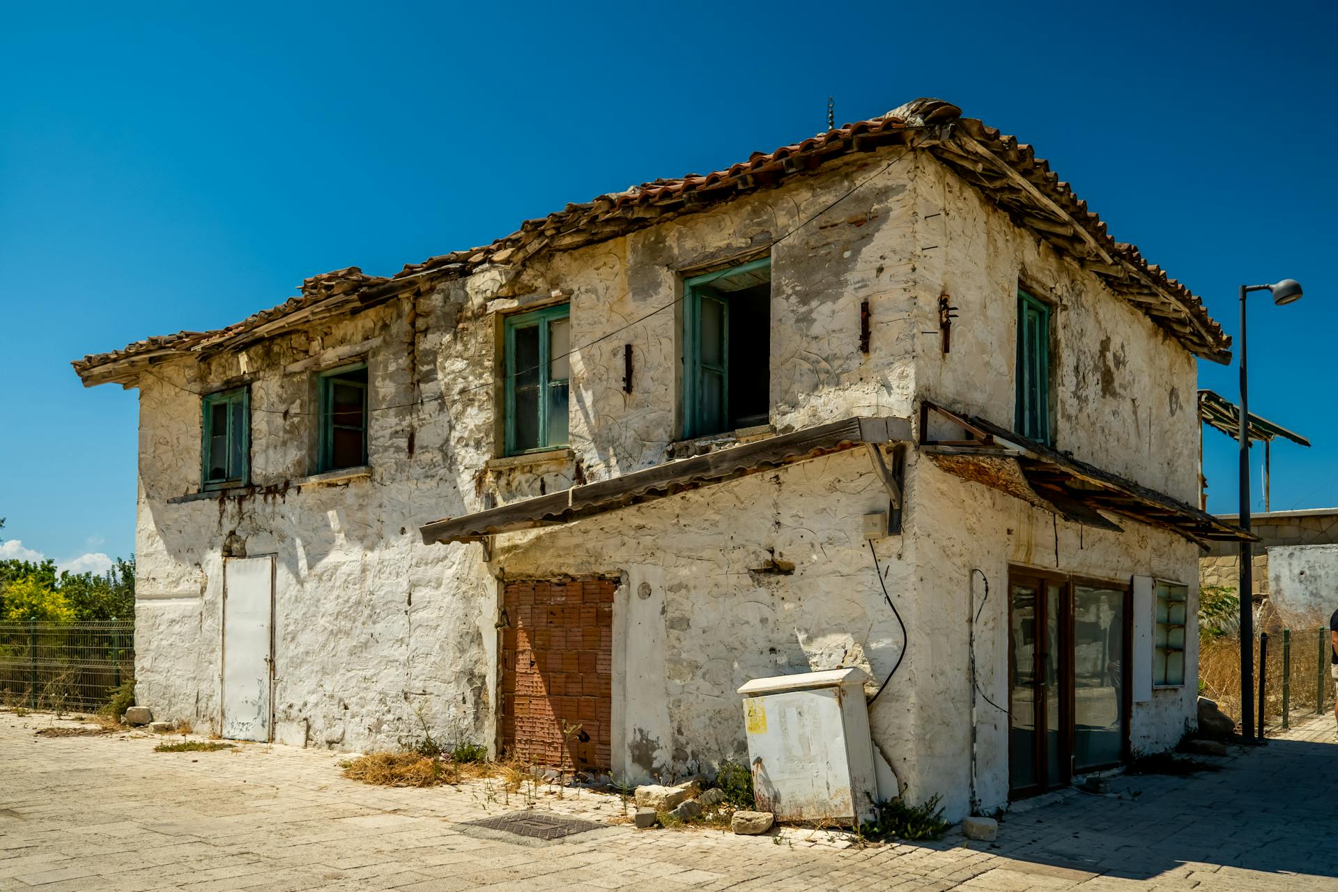 Old, weathered two-story stone building with white walls and damaged roof under clear blue sky.