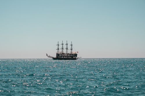 Free A majestic sailing ship glides across a sparkling blue sea under a clear sky. Stock Photo