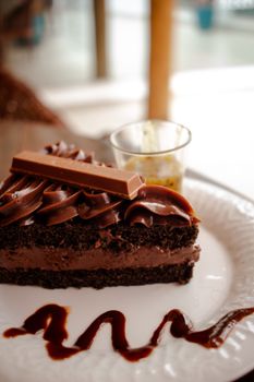 Indulgent chocolate cake slice with frosting and glaze on a white plate.