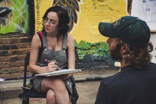 A young artist sketching outdoors surrounded by vibrant graffiti on walls.