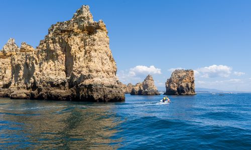 Free Breathtaking view of rocky cliffs along a vibrant blue sea with a small boat under a clear sky. Stock Photo