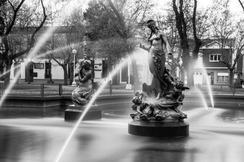 Free A classic black and white photograph featuring an elegant fountain with intricate sculptures in a city square. Stock Photo
