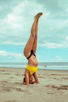 A woman performs a headstand yoga pose on the sandy beach at General Villamil, Ecuador, under a cloudy sky.