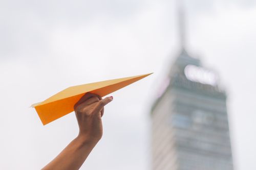 Free Close-up of a hand holding a paper airplane with Torre Latinoamericana in the background, Mexico City. Stock Photo