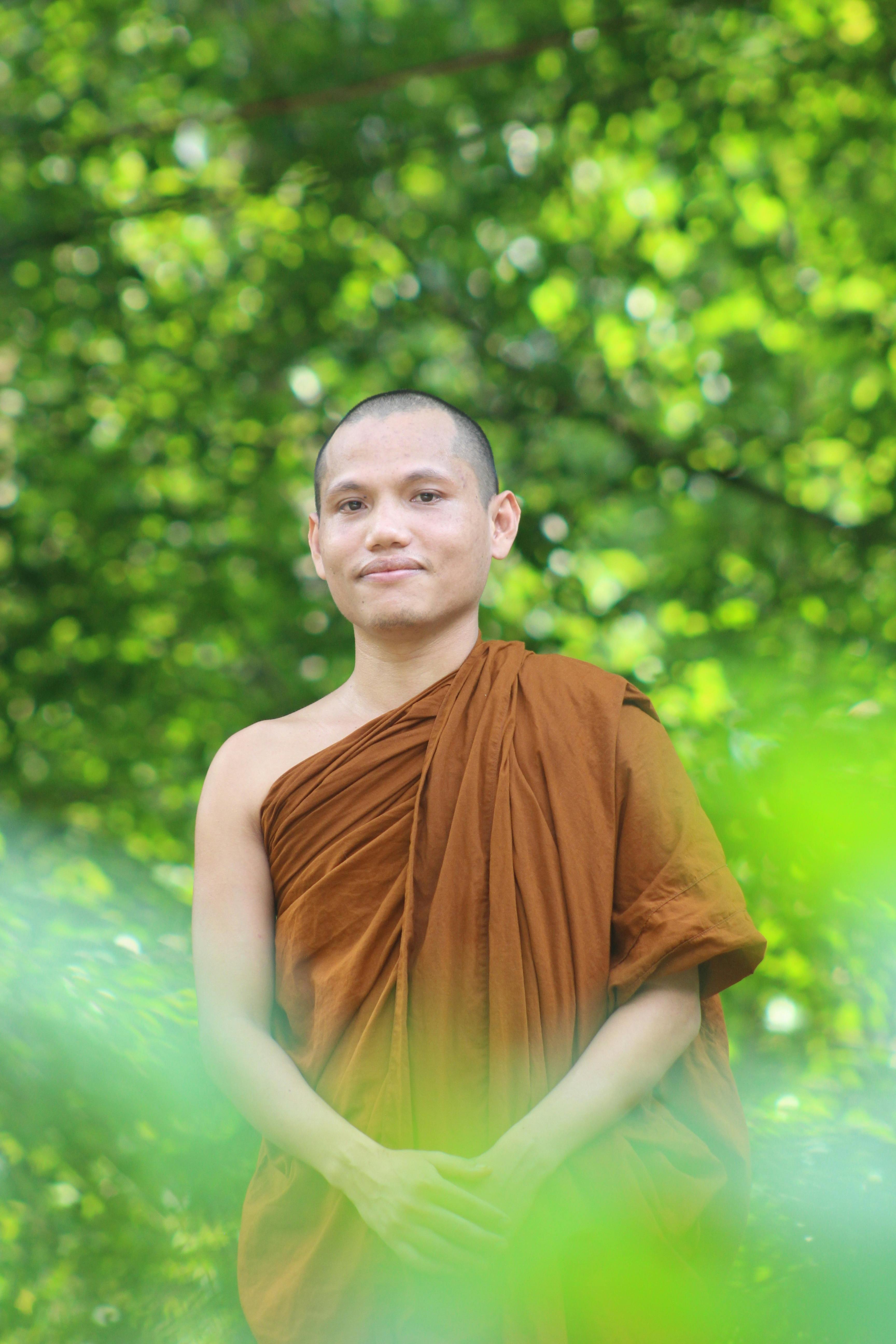 Buddhist monk in traditional robe standing amidst lush greenery.
