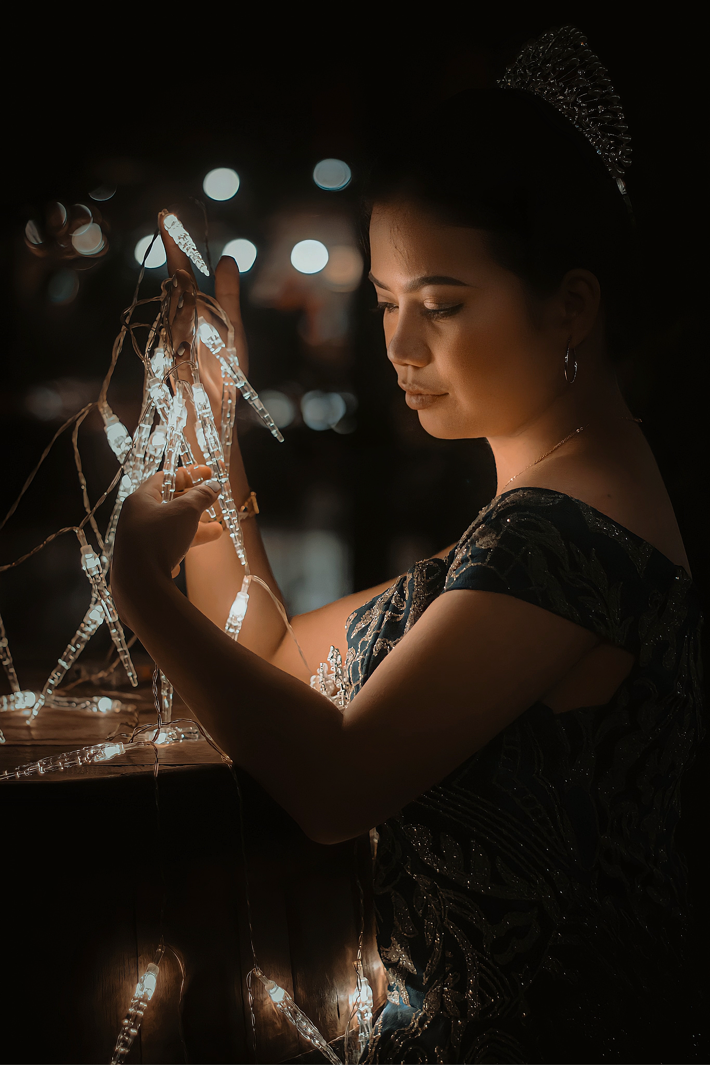 A woman in a ball gown elegantly holds glowing string lights, creating a magical ambiance.