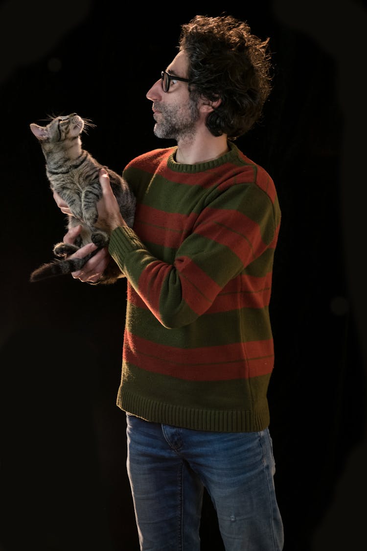 A Man In Red And Green Sweater Carrying A Cat