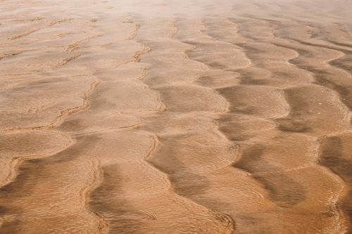 Free Close-up view of sandy beach with natural wave patterns reflecting sunlight. Stock Photo