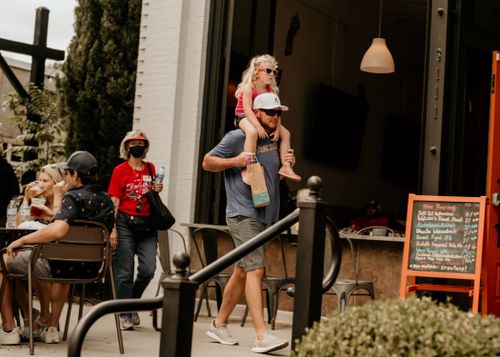 Free A father carrying his daughter on shoulders outside a cafe, enjoying a sunny day. Stock Photo