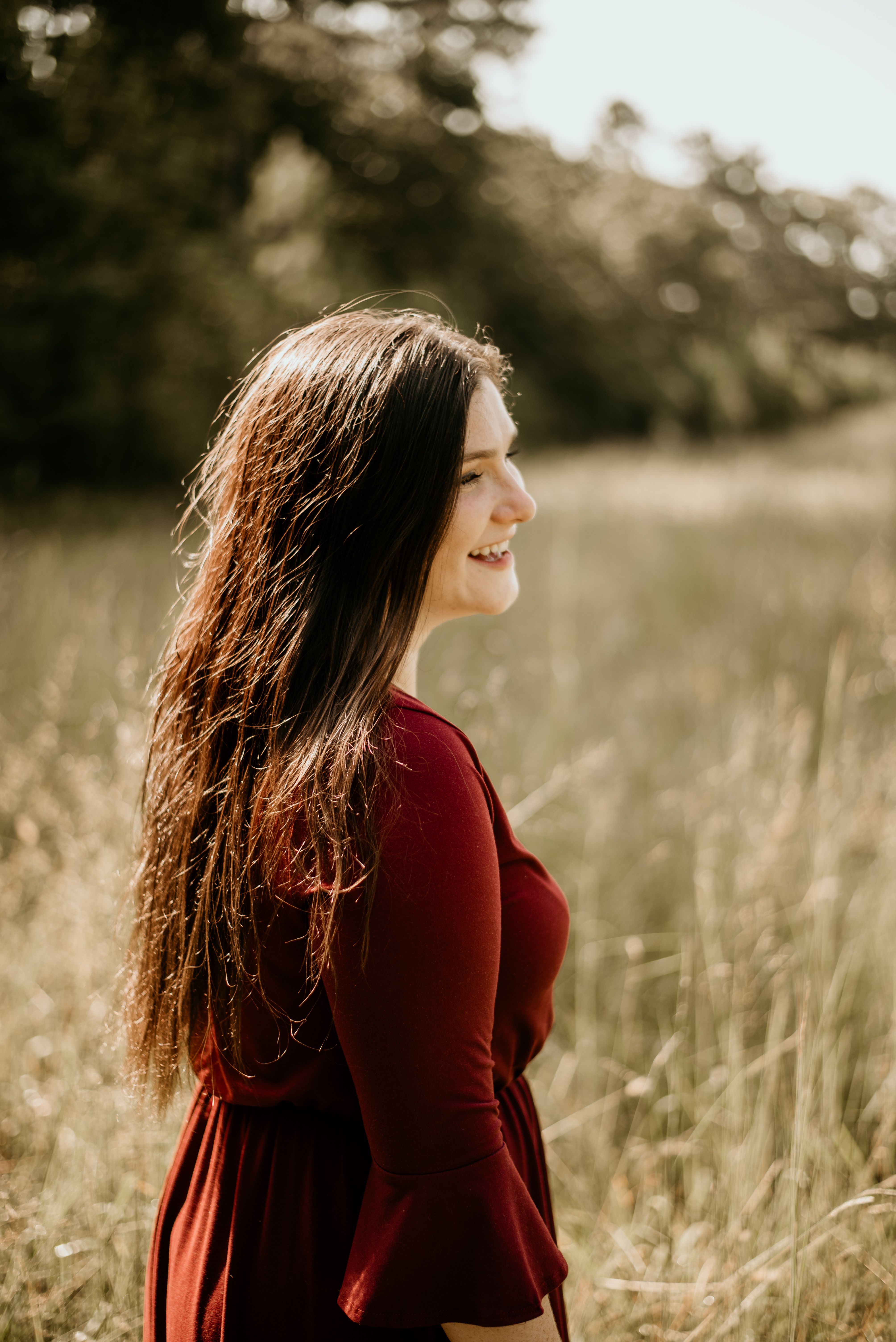 A woman in a red dress smiling in a sunlit meadow, exuding happiness.