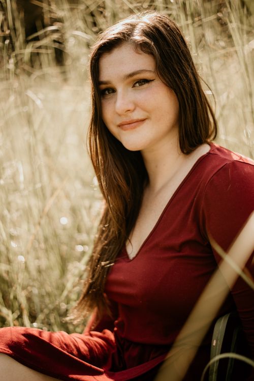 Free A young woman smiling while sitting in a sunny field wearing a red top. Stock Photo