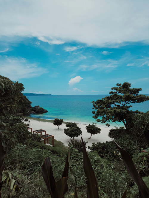 Free Stunning tropical beach with clear blue waters and lush greenery under a bright sky. Stock Photo