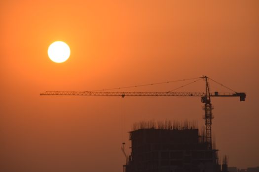 A striking silhouette of a construction crane set against a vibrant sunset sky in Faridabad, India.