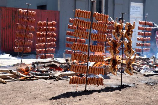 Rows of sausages and chickens roasting on open fire, creating a vibrant outdoor barbecue scene.
