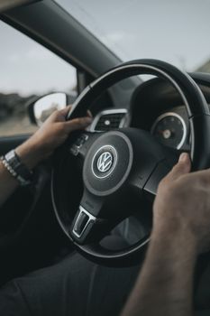Hands gripping a Volkswagen steering wheel in a car interior close-up shot.
