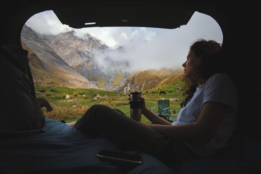 A woman enjoys a serene moment from her tent, gazing at a breathtaking mountain view.