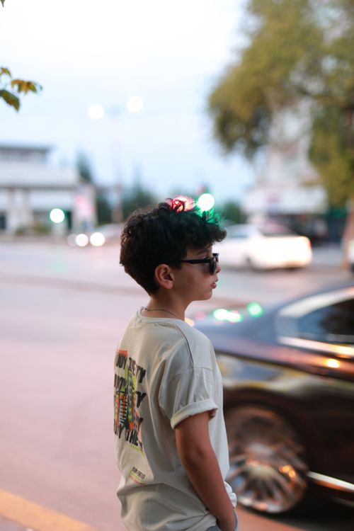 Free A stylish child wearing sunglasses stands on a city street, captured with a blurred urban background. Stock Photo