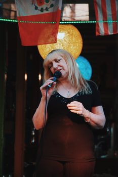 Blonde woman sings passionately into a microphone, set against vibrant lighting in CABA, Argentina.