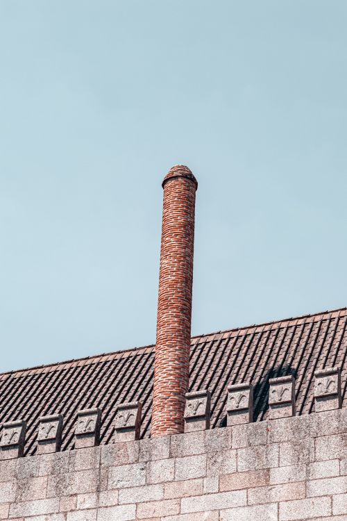 Free A low angle view of a brick chimney on a building with a tiled roof under a clear blue sky. Stock Photo