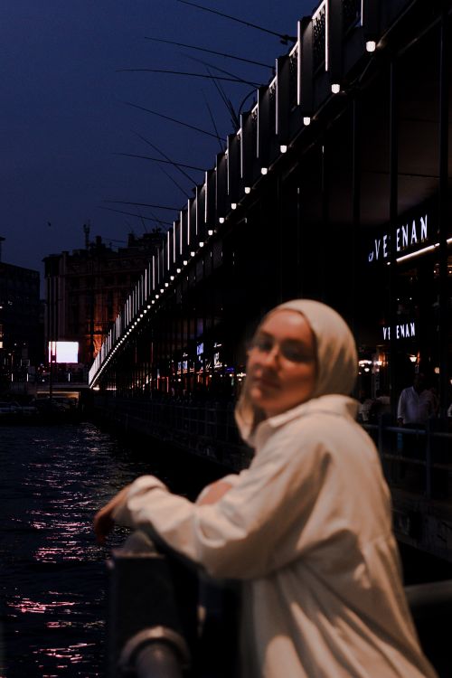 Free A woman in a hijab poses near a lit bridge at night, creating a serene, urban atmosphere. Stock Photo