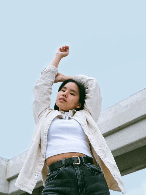 Free Stylishly dressed woman confidently poses outdoors with arms raised, embracing freedom. Stock Photo