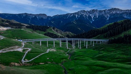 Free Aerial photo of a bridge spanning a lush green valley in Ili, Xinjiang, China, with mountain backdrop. Stock Photo