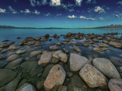 Tranquil scene of a rocky shoreline with clear waters and a dramatic sky.