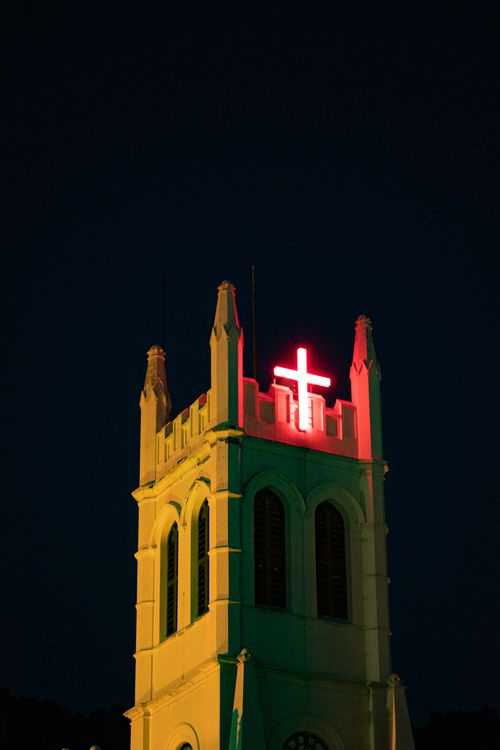 Free Night view of a church tower with a glowing red cross against a dark sky. Stock Photo