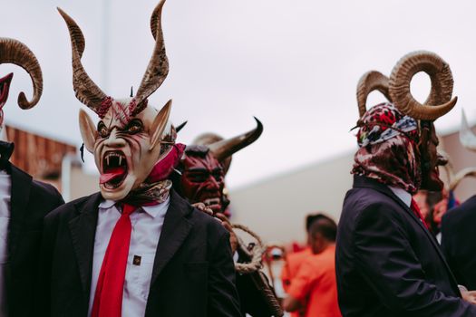 Men in elaborate devil masks perform a traditional folk dance outdoors.