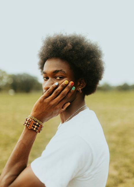 A young man in a t-shirt with colorful nails poses playfully outdoors.