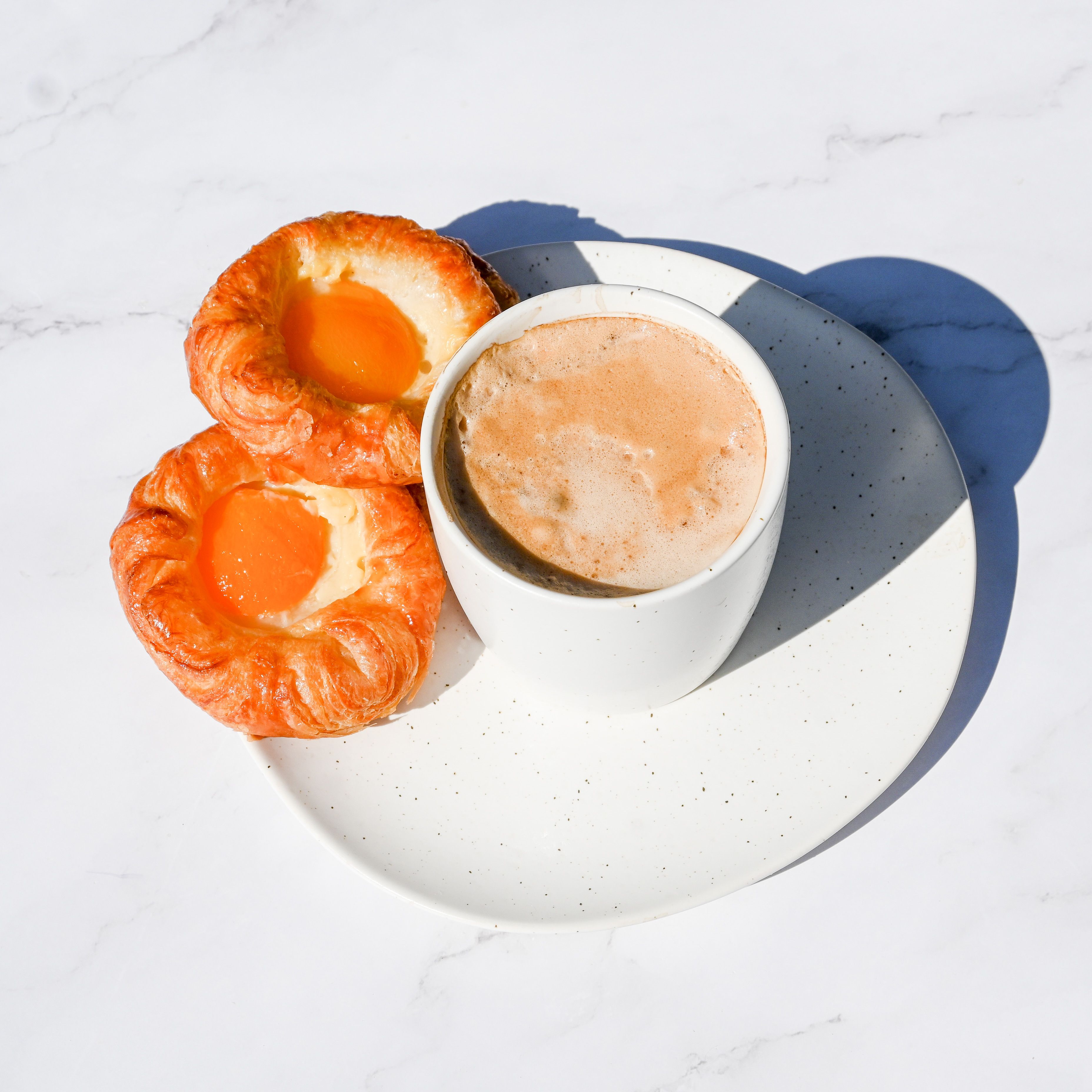 Close-up of pastries with apricot jam and a cup of coffee on a white plate.