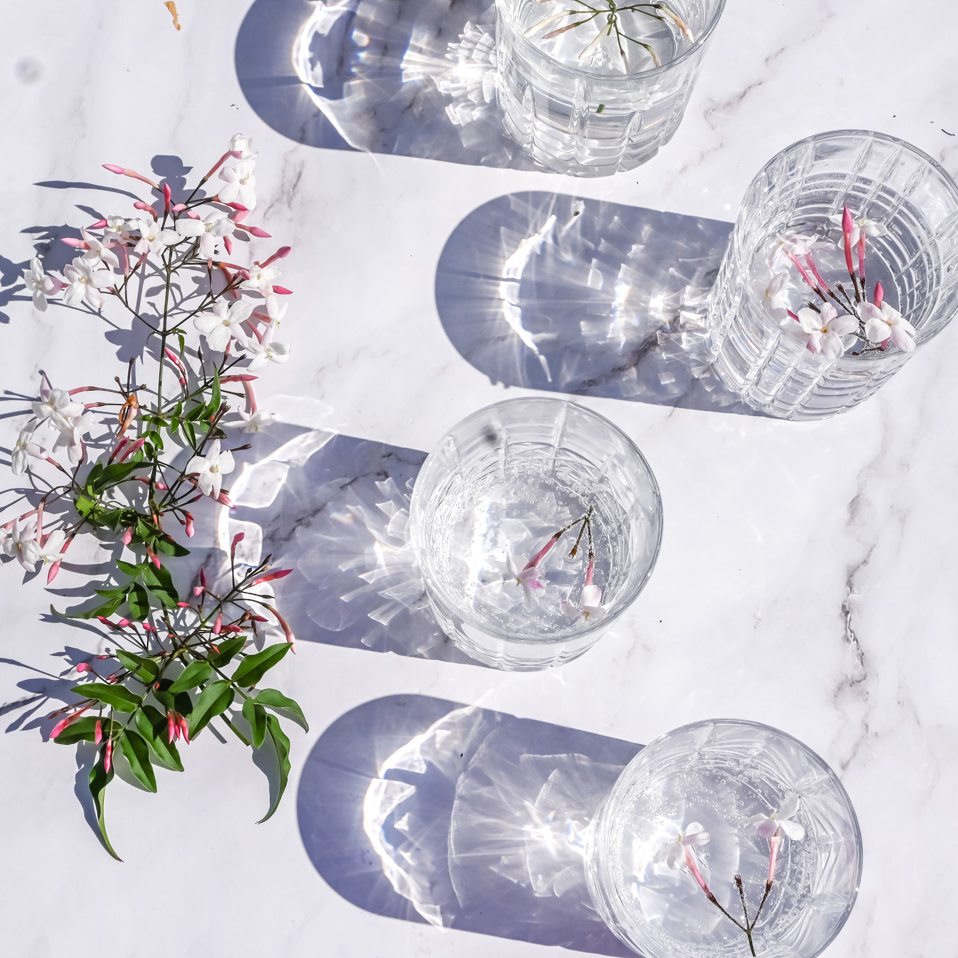 Crystal glasses with water and jasmine create beautiful light and shadow patterns on a marble surface.