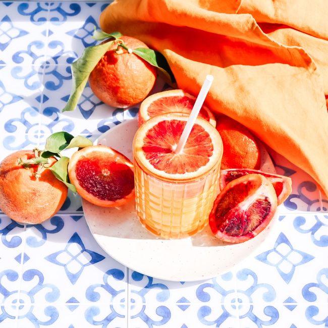 Vibrant blood orange juice with fresh slices on blue Moroccan tiles, perfect for summer refreshment.
