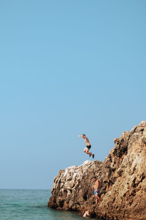 Free Man jumps from rocky cliff into the ocean at Vlorë County, Albania, a thrilling summer adventure. Stock Photo