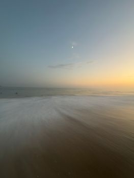 Serene seascape at dusk with gentle waves and a visible moon in the sky.