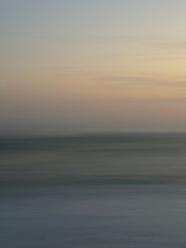 Soft and tranquil seascape at sunset with blurred ocean waves and a pastel sky.