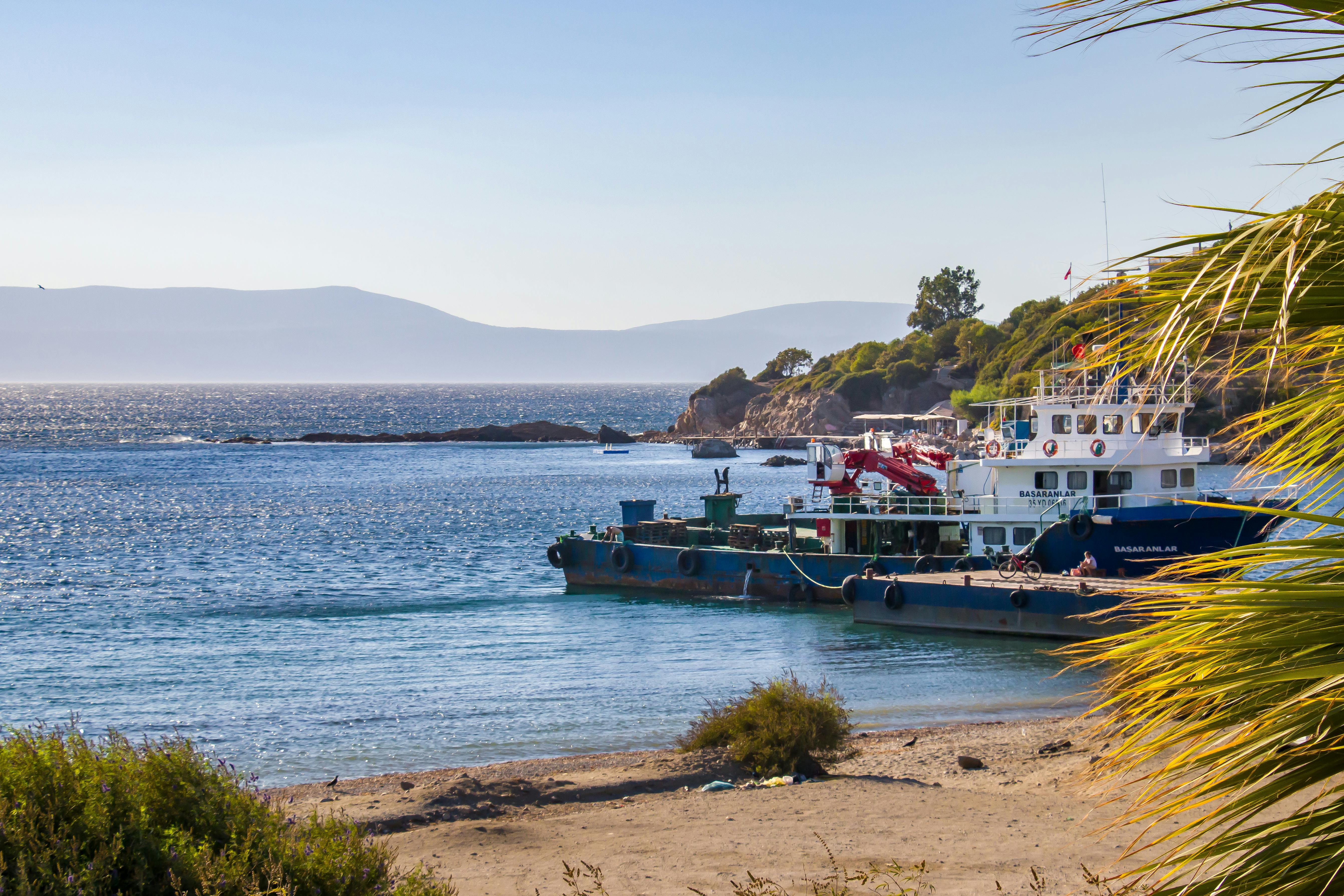 Free Tranquil coastal scene featuring a cargo ship anchored at the shore under clear blue skies. Stock Photo