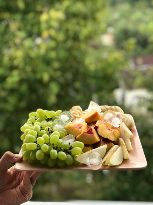 Free Hand holding a vibrant platter of grapes, peaches, and pears outdoors, perfect for a healthy snack. Stock Photo
